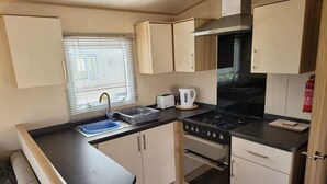 Una kitchenette compacta con un fregadero, estufa y horno, y una ventana con persianas.