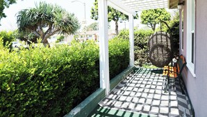 Une véranda couverte avec un sol à carreaux, un banc et une cage à oiseaux suspendue.