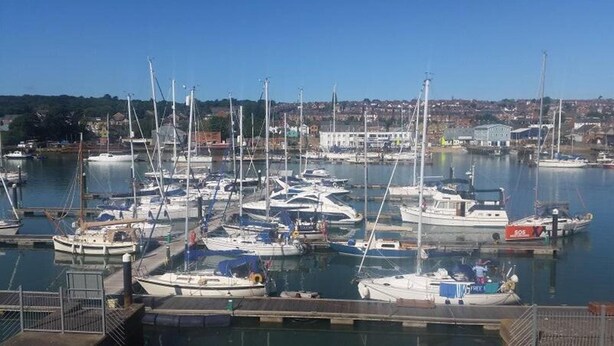 A marina with multiple boats docked, a clear sky, and a residential area in the background. - Marina View, South Facing Balcony Sunny Apartment (East Cowes)