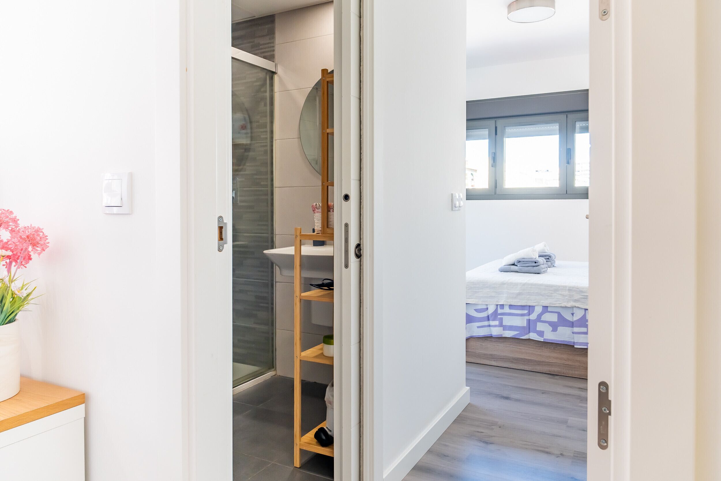 Un baño con cabina de ducha de vidrio, estante de madera y lavamanos blanco.