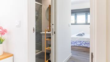 Un baño con cabina de ducha de vidrio, estante de madera y lavamanos blanco.