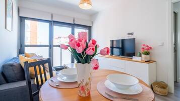 Una cocina moderna con una mesa de comedor para dos personas, un jarrón con flores rosadas y un televisor sobre la encimera.