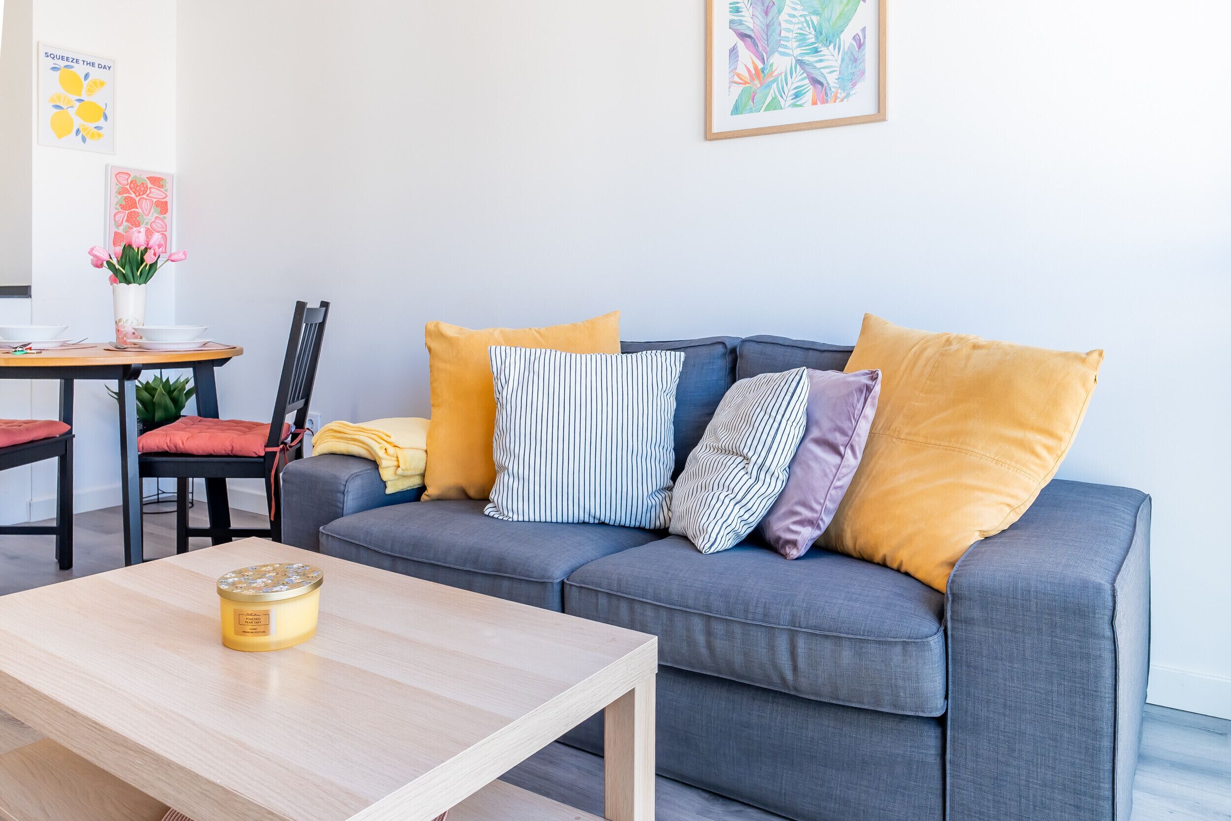 Una sala de estar moderna con un sofá gris, varios cojines, una mesa de centro de madera y una zona de comedor con una silla y una mesa.