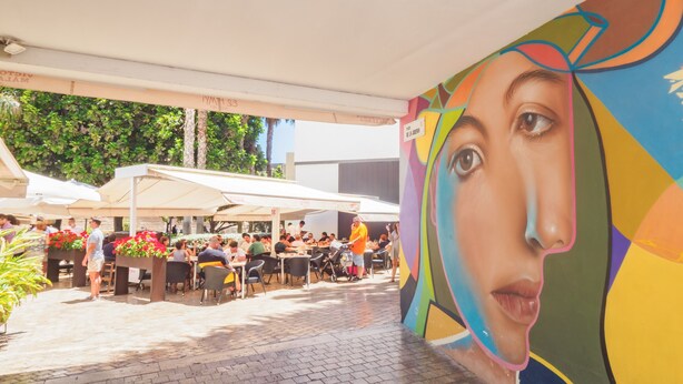 An outdoor dining area with tables and chairs, surrounded by a mural.