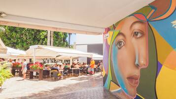 Un área de comedor al aire libre con mesas y sillas, rodeada por un mural.
