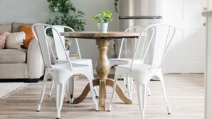 Un coin repas avec une table ronde en bois entourée de quatre chaises blanches. Une plante en pot est posée sur la table.