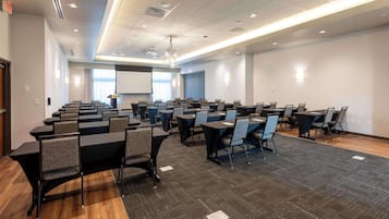 A conference room with multiple tables and chairs, a projector screen, and a large window with curtains.