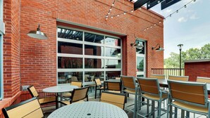 An outdoor patio with round tables and chairs, a brick wall, and string lights. - Drury Plaza Hotel Savannah Pooler (Pooler)