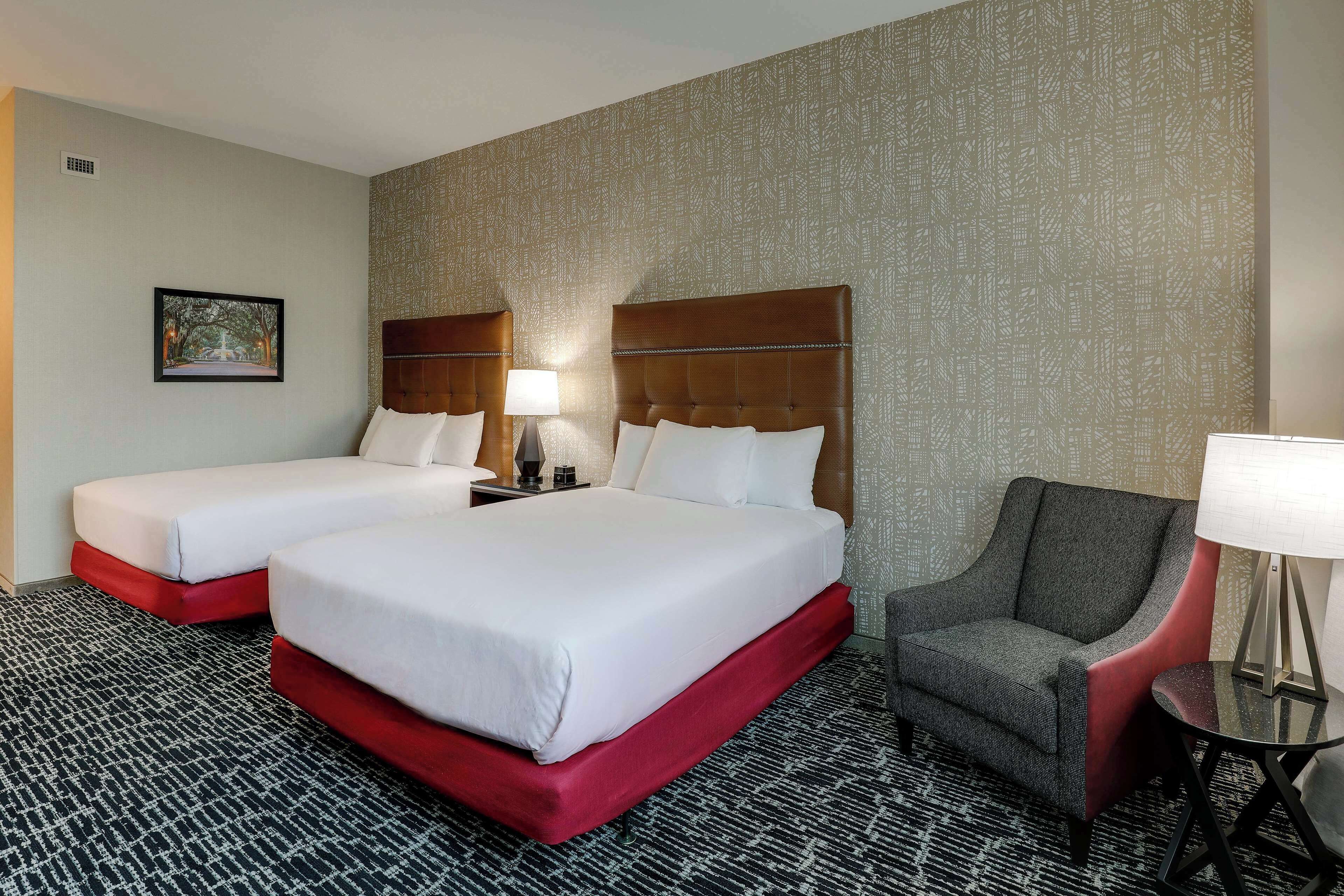 A hotel room with two beds, a chair, and a small table.
