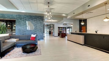 Um hall amplo com uma recepção moderna, área de estar com sofá e mesa de centro, e um grande lustre.
