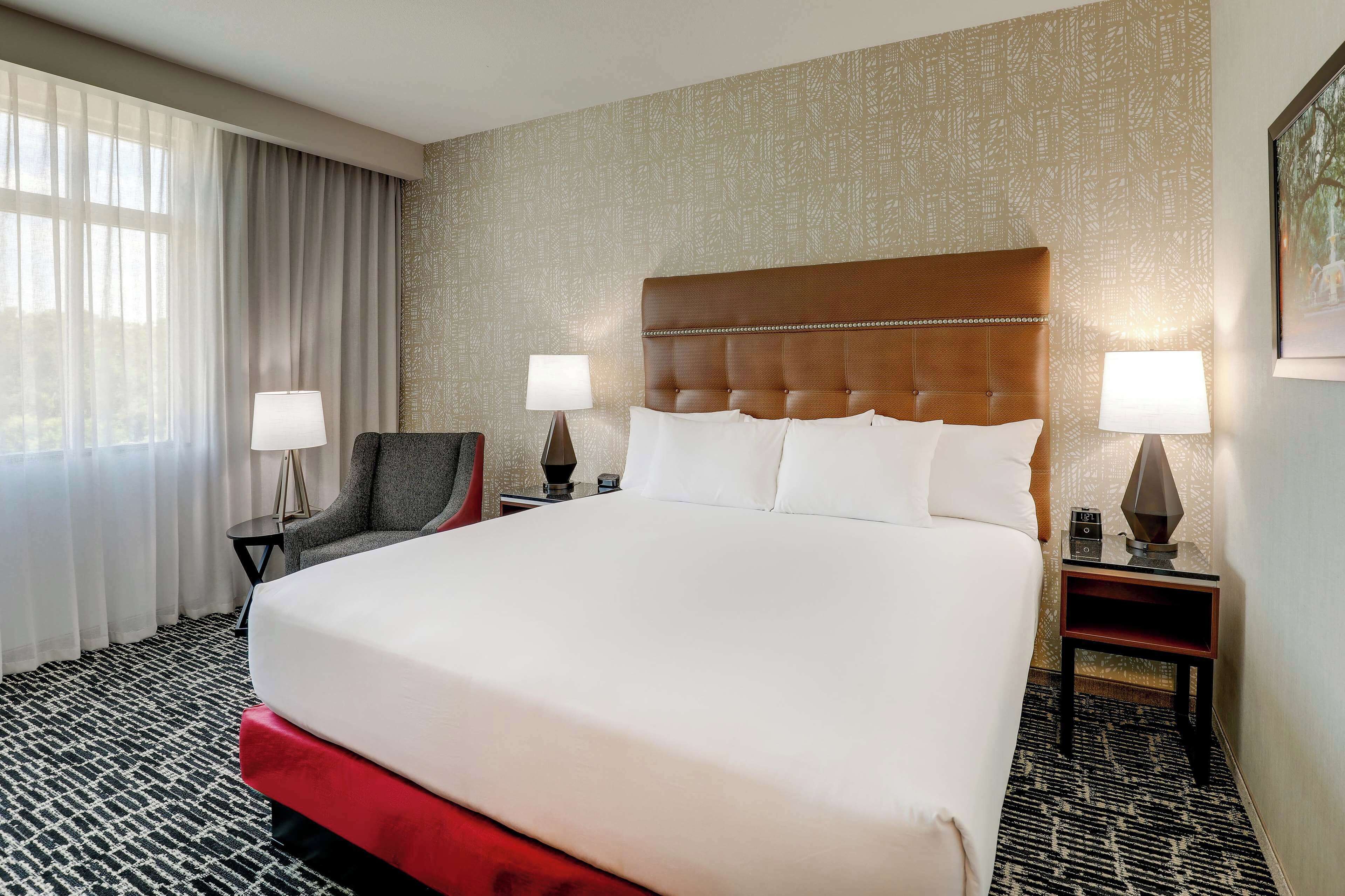A hotel room with a large bed, two bedside tables with lamps, a chair, and a patterned carpet.