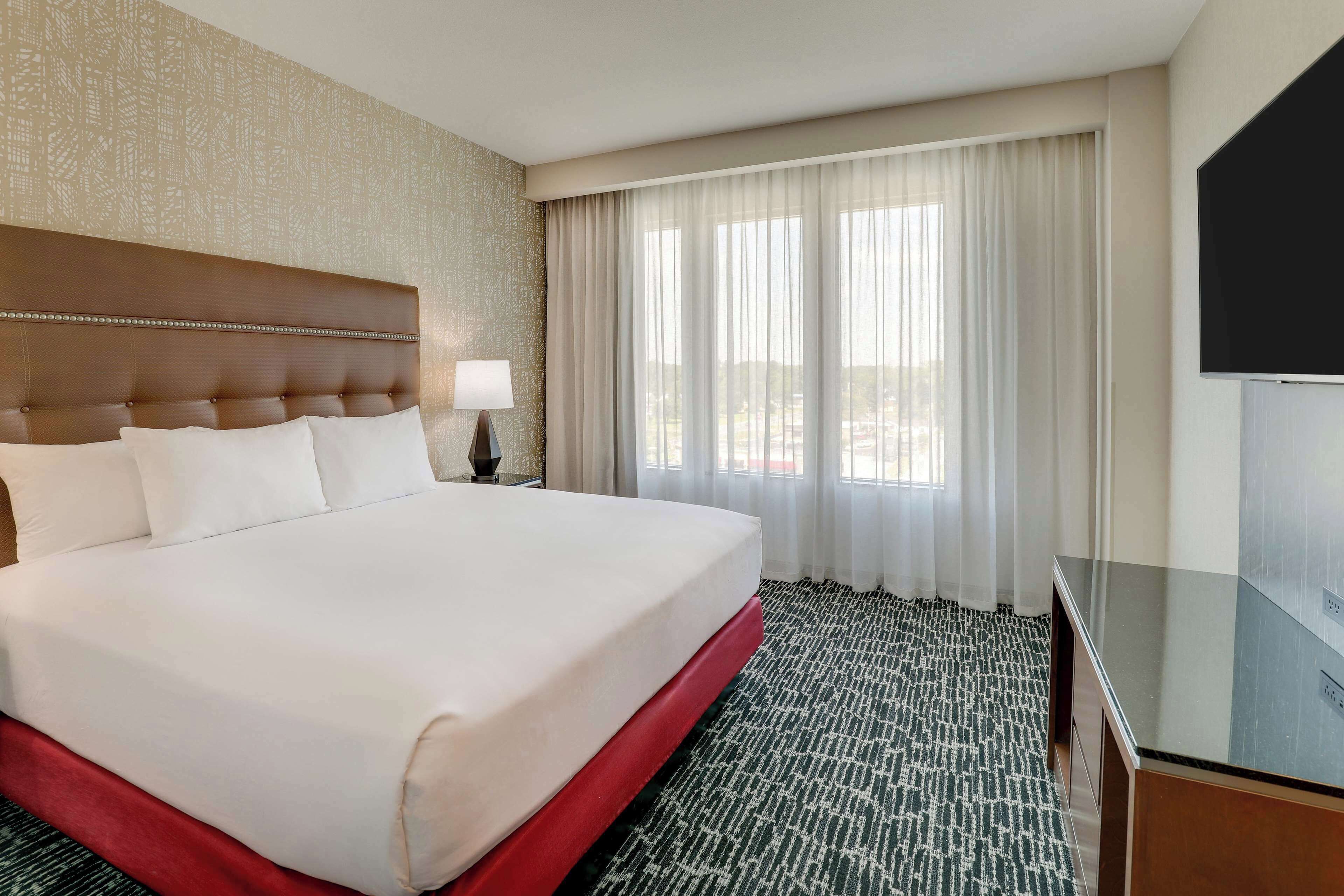 A hotel room with a large bed, a TV, and a view of the outdoors through the window.