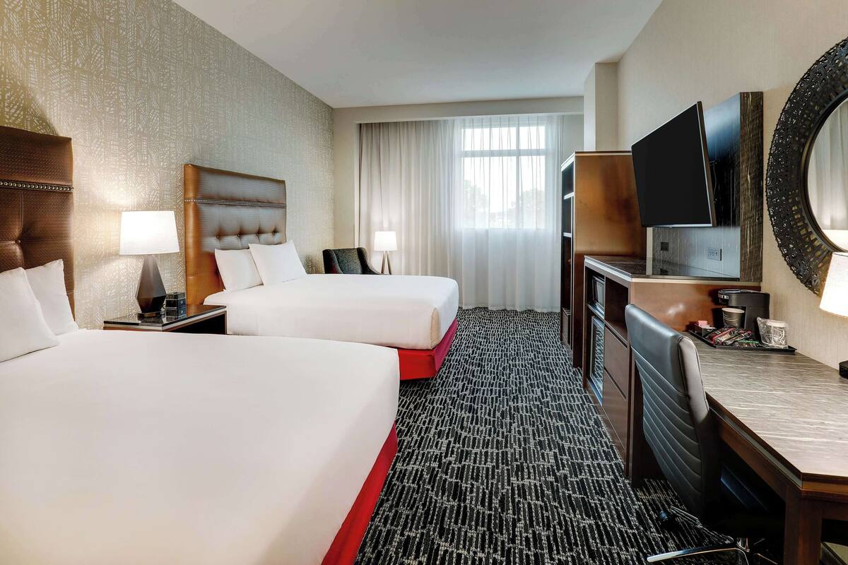 A hotel room with two beds, a desk, a TV, and a large mirror.