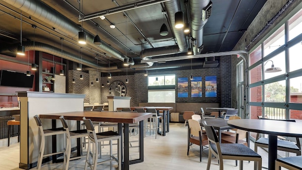 A modern cafe with exposed ductwork, a brick wall, and large windows. - Drury Plaza Hotel Savannah Pooler (Pooler)