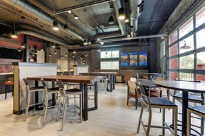 Un café moderne avec des conduits apparents, un mur en briques et de grandes fenêtres.