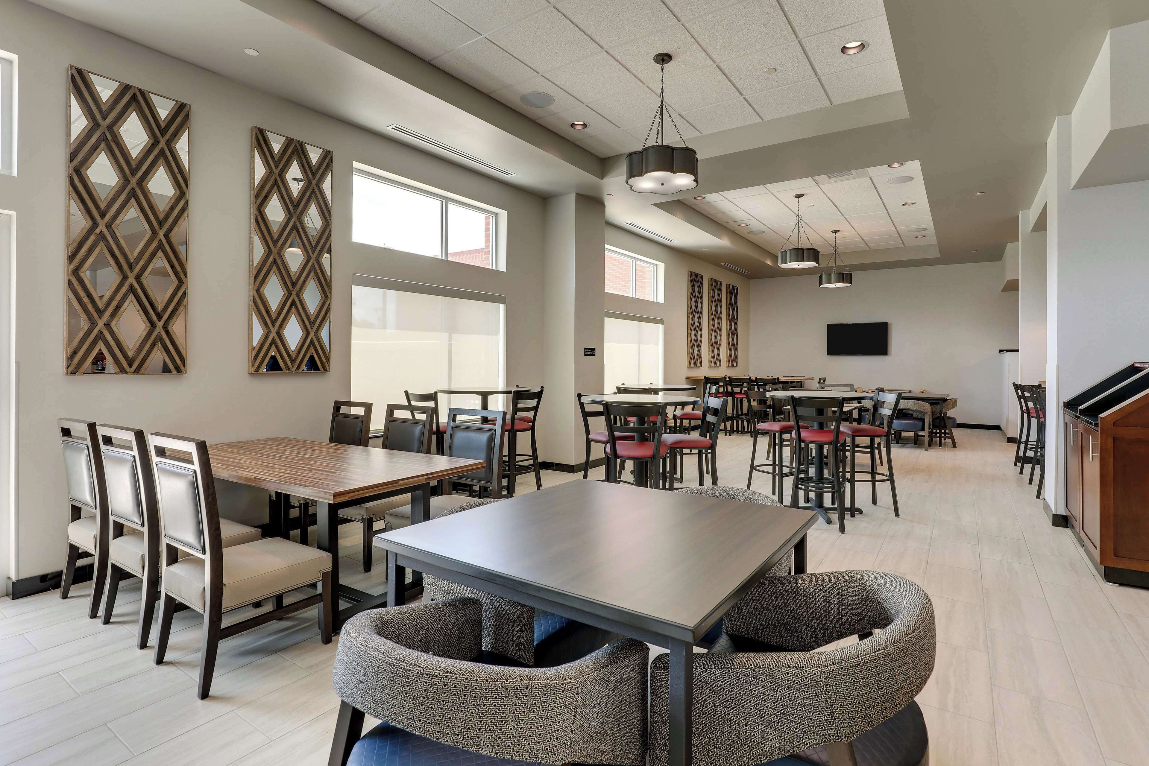 A spacious dining area with multiple tables and chairs, large windows, and decorative wall panels.