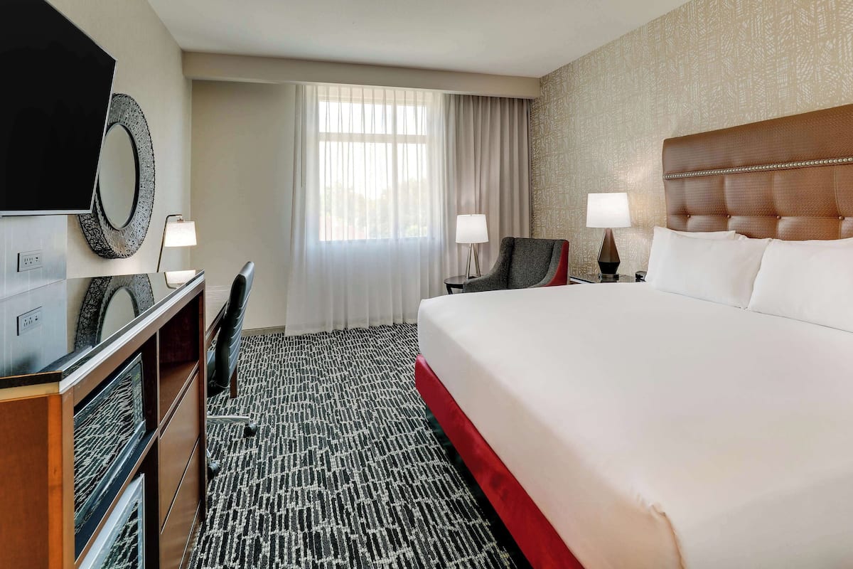 A hotel room with a large bed, a desk with a chair, a TV, and two bedside lamps.