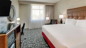 A hotel room with a large bed, a desk with a chair, a TV, and two bedside lamps.