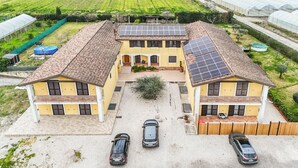 Ein zweistöckiges, gelbes Gebäude mit Ziegeldach, Solaranlagen und einer Auffahrt mit vier Autos.