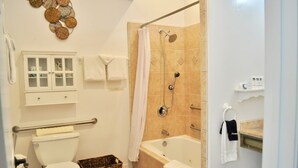 A bathroom with a toilet, a shower, a bathtub, a wicker basket, a towel rack, and a cabinet with glass doors. - Queen downstairs room (cayucos)