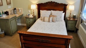 A neatly arranged bedroom with a large bed, two bedside tables with lamps, a small desk with a telephone and a clock, and a cabinet with various items. - Queen downstairs room (cayucos)