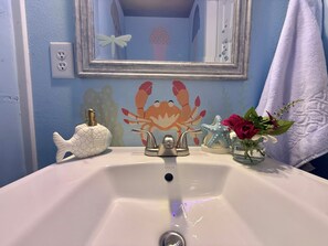 Un baño con lavamanos, espejo, decoración de cangrejo, una estrella de mar y un florero con flores.