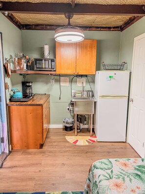 A compact kitchen with wooden cabinets, a microwave, a coffee maker, and a refrigerator.
