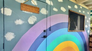 Una puerta con un mural de arcoíris, un cartel que solicita quitarse los zapatos y una ventana con vistas.