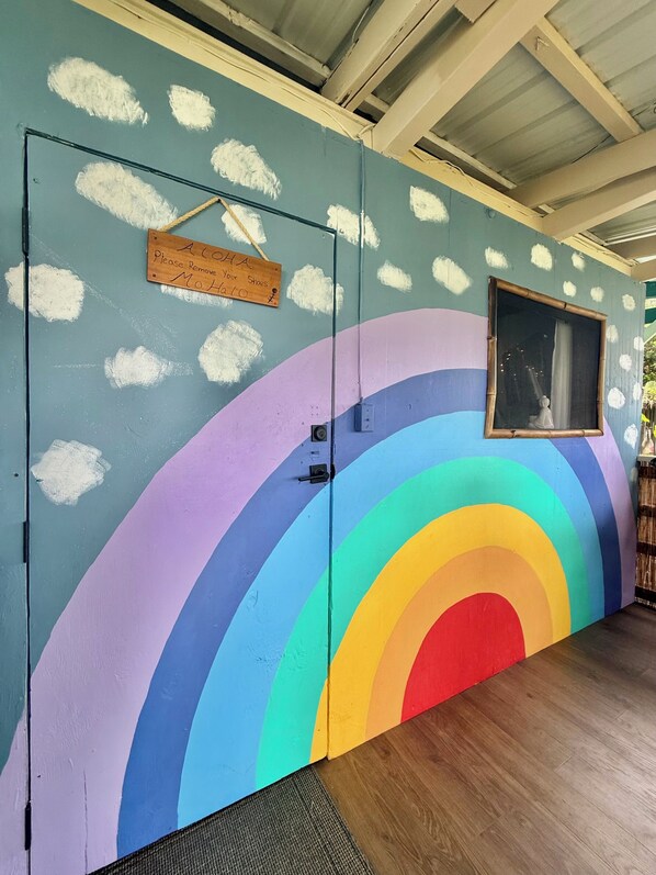 Una puerta con un mural de arcoíris, un cartel que solicita quitarse los zapatos y una ventana con vistas.