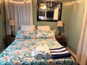 Un dormitorio con cama, dos mesitas de noche, un espejo y luces de hadas.