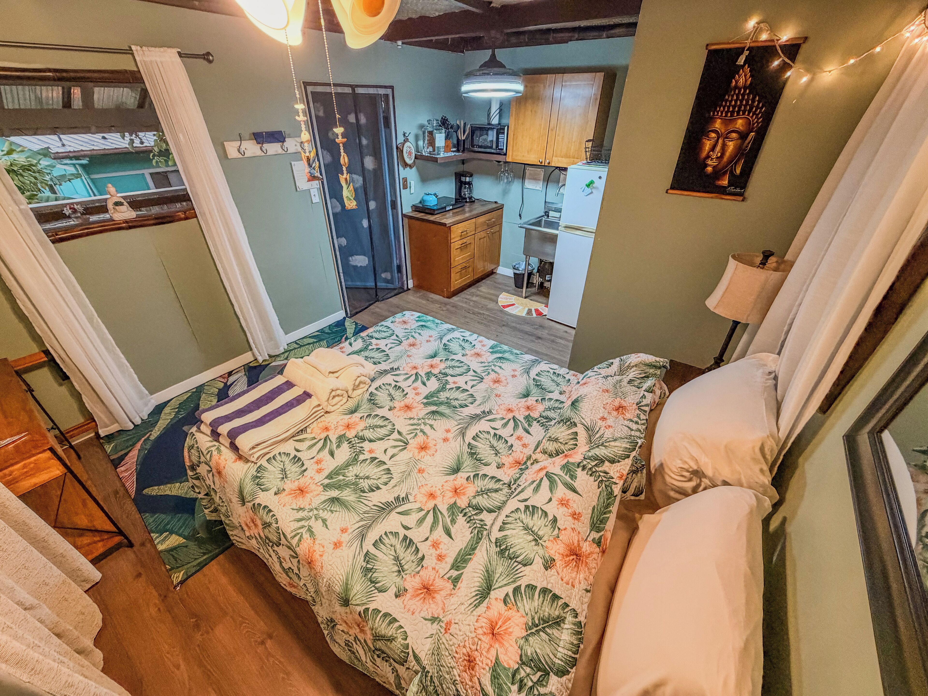 Un dormitorio con cama, mesita de noche, ventana con cortinas, puerta y vista al exterior.