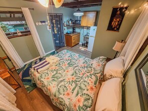 A bedroom with a bed, a nightstand, a window with curtains, a door, and a view of the outside.