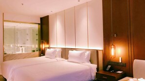 Habitación de hotel con una cama grande, una mesita de noche con un teléfono y una bandeja de té, un espejo y una lámpara de pared.