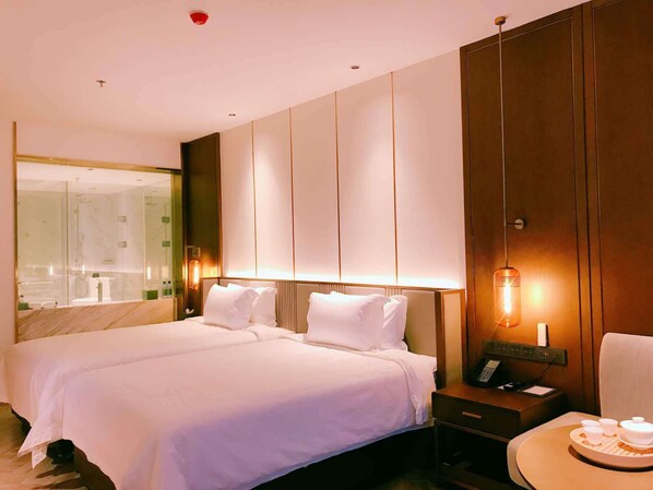 Habitación de hotel con una cama grande, una mesita de noche con un teléfono y una bandeja de té, un espejo y una lámpara de pared.