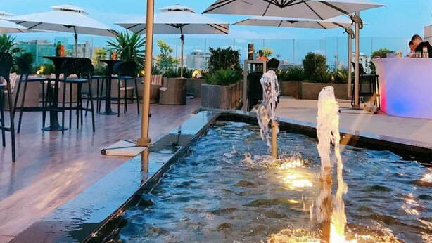 Un espacio al aire libre con mesas, sombrillas, una fuente de agua y un bar.