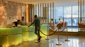 Un moderno vestíbulo de hotel con mostrador de recepción, zona de estar y grandes ventanales que ofrecen vistas a la ciudad.