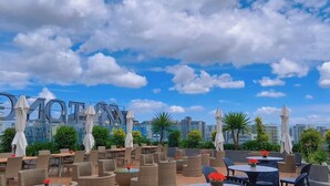 Un área de estar al aire libre con sombrillas y mesas, con vistas a un paisaje urbano de edificios y palmeras.