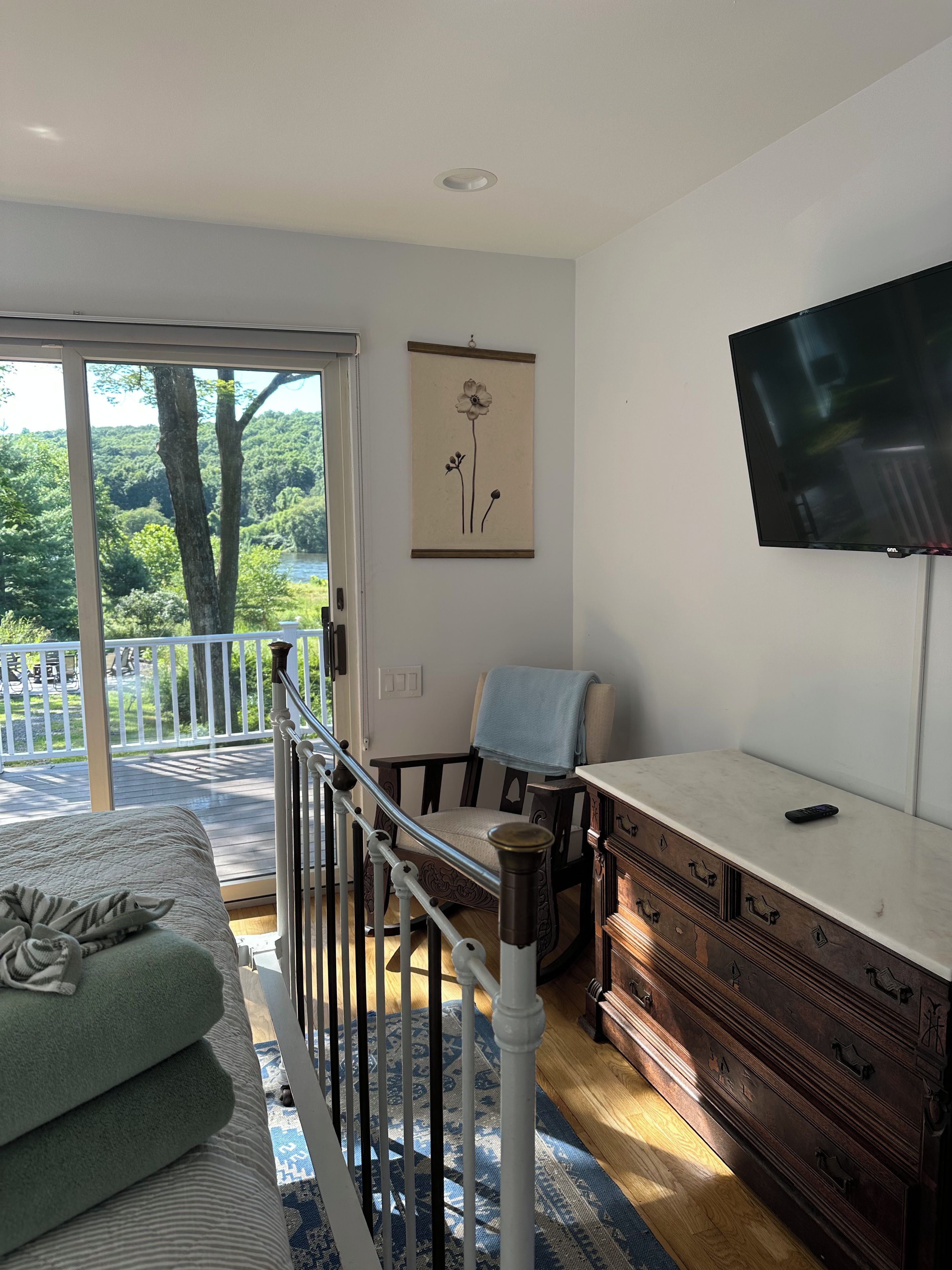 A bedroom with a bed, a chair, a dresser, a television, and a window with a view of trees.