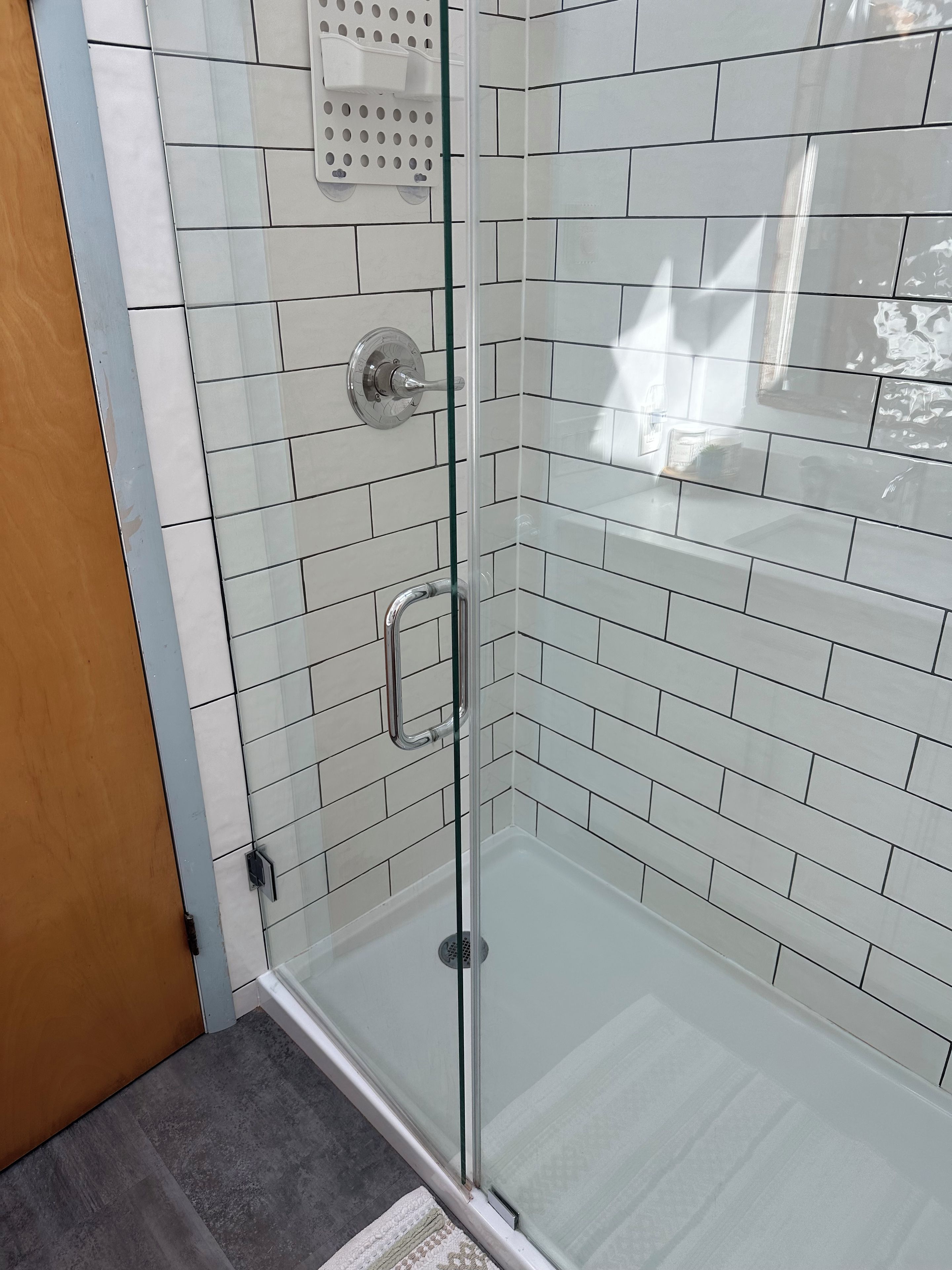 Een douche met glazen wanden, witte metro tegels, een handdouche en bedieningspaneel.