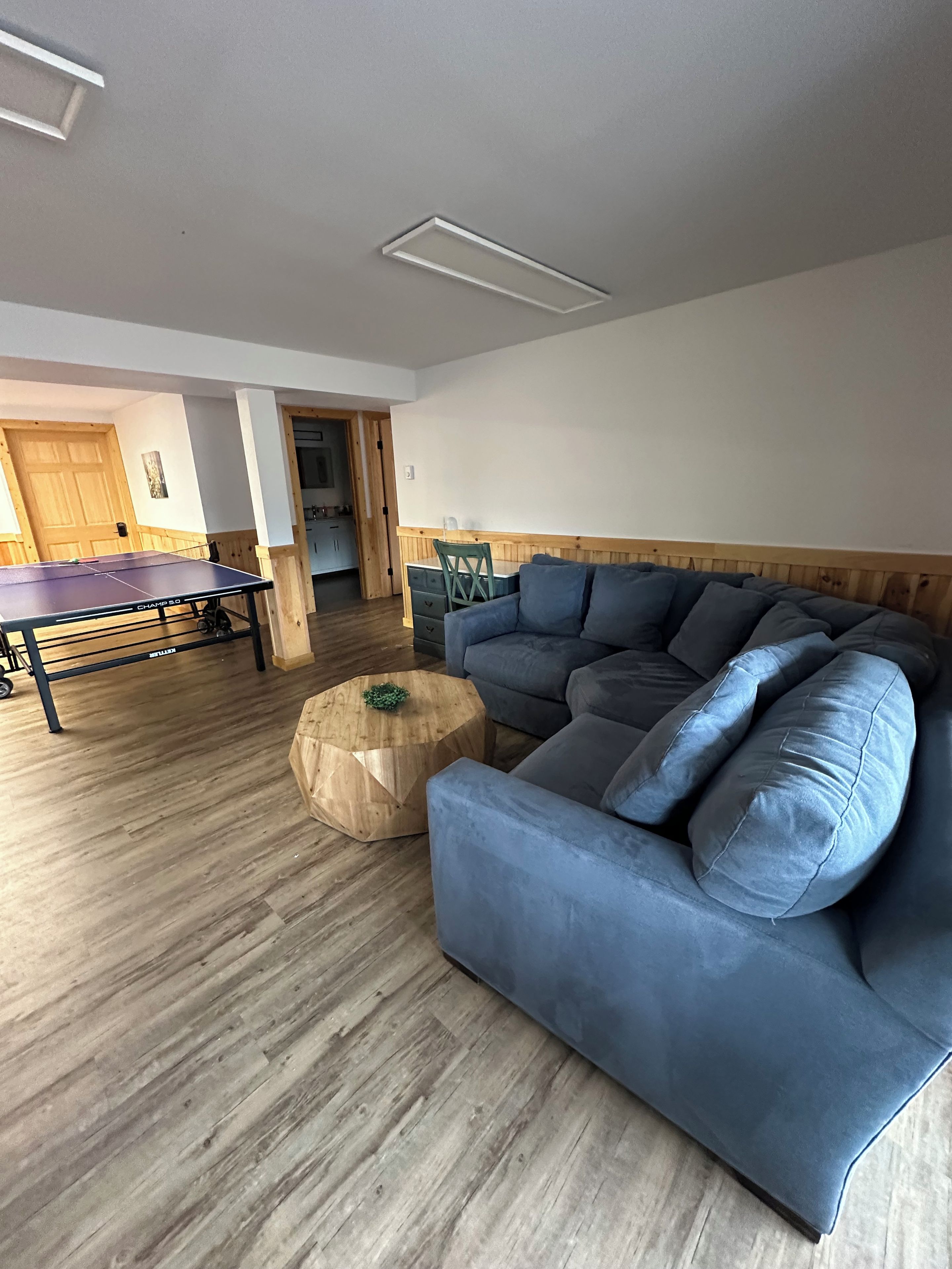Een woonkamer met een blauwe bank, een tafeltennistafel en een houten salontafel.