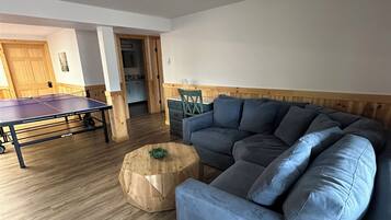 Een woonkamer met een blauwe bank, een tafeltennistafel en een houten salontafel.