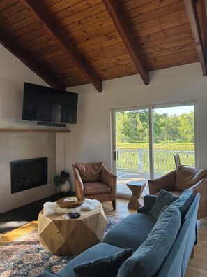A living room with a fireplace, a television mounted on the wall, and a large window offering a view of a balcony.
