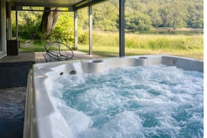 A hot tub with a wooden deck and a view of a grassy field and trees. - Entire Home on Delaware River! Hot Tub & Game Room! (Narrowsburg)