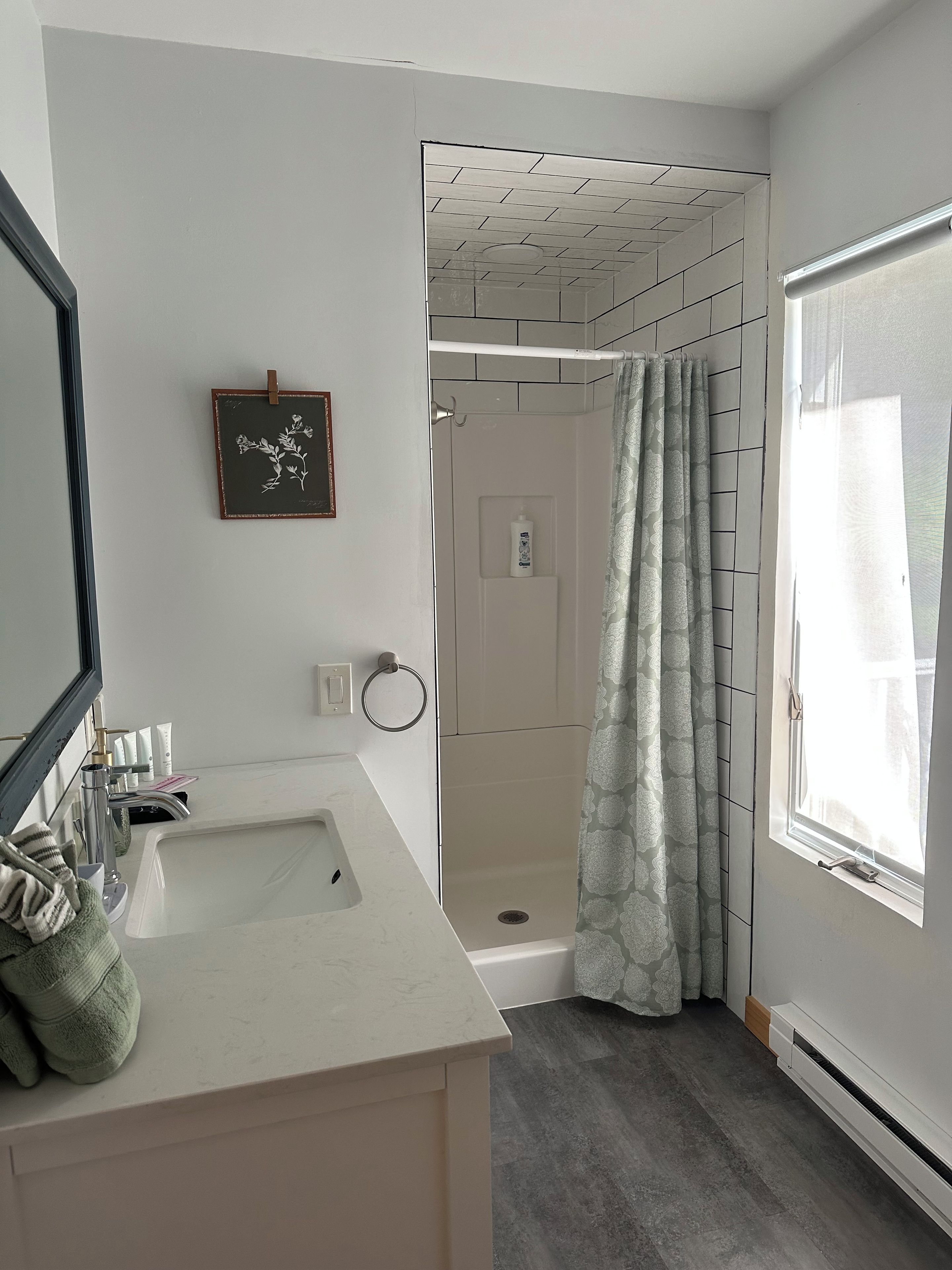 Une salle de bain avec un lavabo blanc, une douche et une fenêtre.
