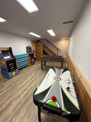 A room with a foosball table, arcade games, and a ping pong table.