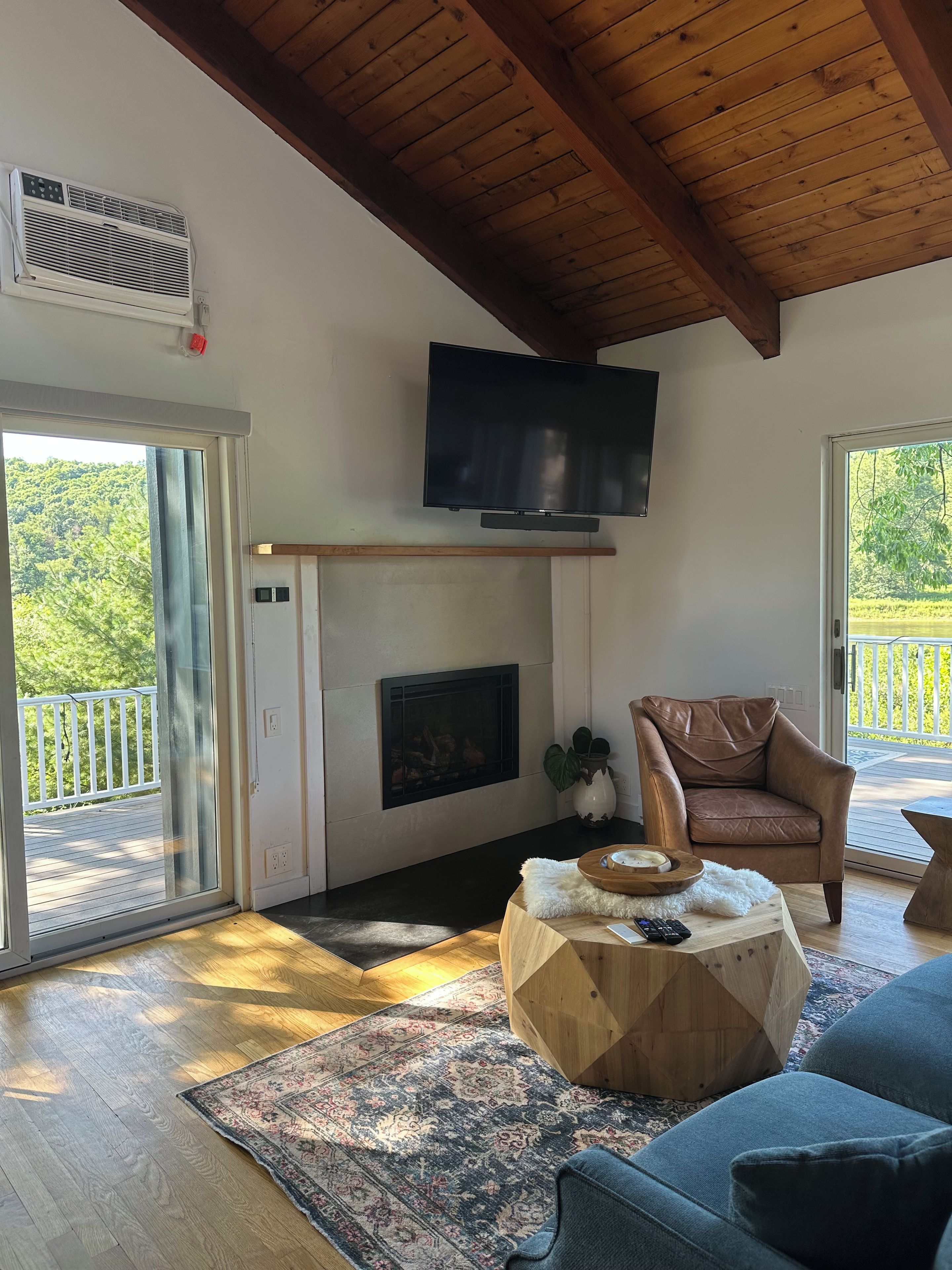 Ein Wohnzimmer mit Kamin, Fernseher, einer Couch und Blick ins Freie.