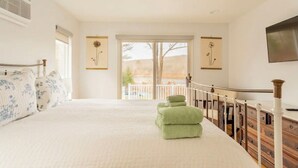 Een slaapkamer met een groot bed, een balkon met uitzicht en twee ingelijste foto’s aan de muur.