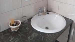 A bathroom with a white sink, a mirror, and a small basket with toiletries. - Rosewood Safari Cottages (Kasane)
