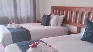 A hotel room with two beds, each with neatly folded white towels and pink flowers. - Rosewood Safari Cottages (Kasane)