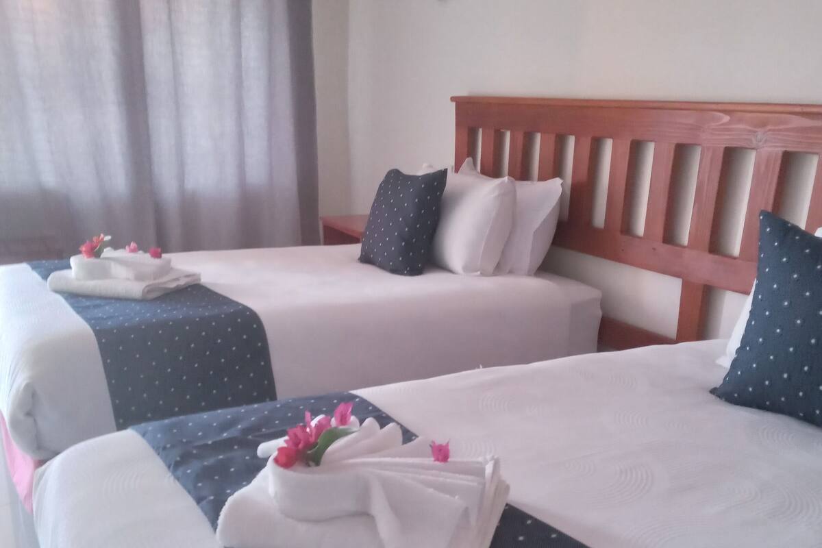 Habitació d'hotel amb dos llits, cadascun amb tovalloles blanques ben arremegades i flors roses.